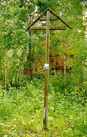 Крест на месте, где похоронены Григорий и Кассиан. За деревьями просматривается колокольня